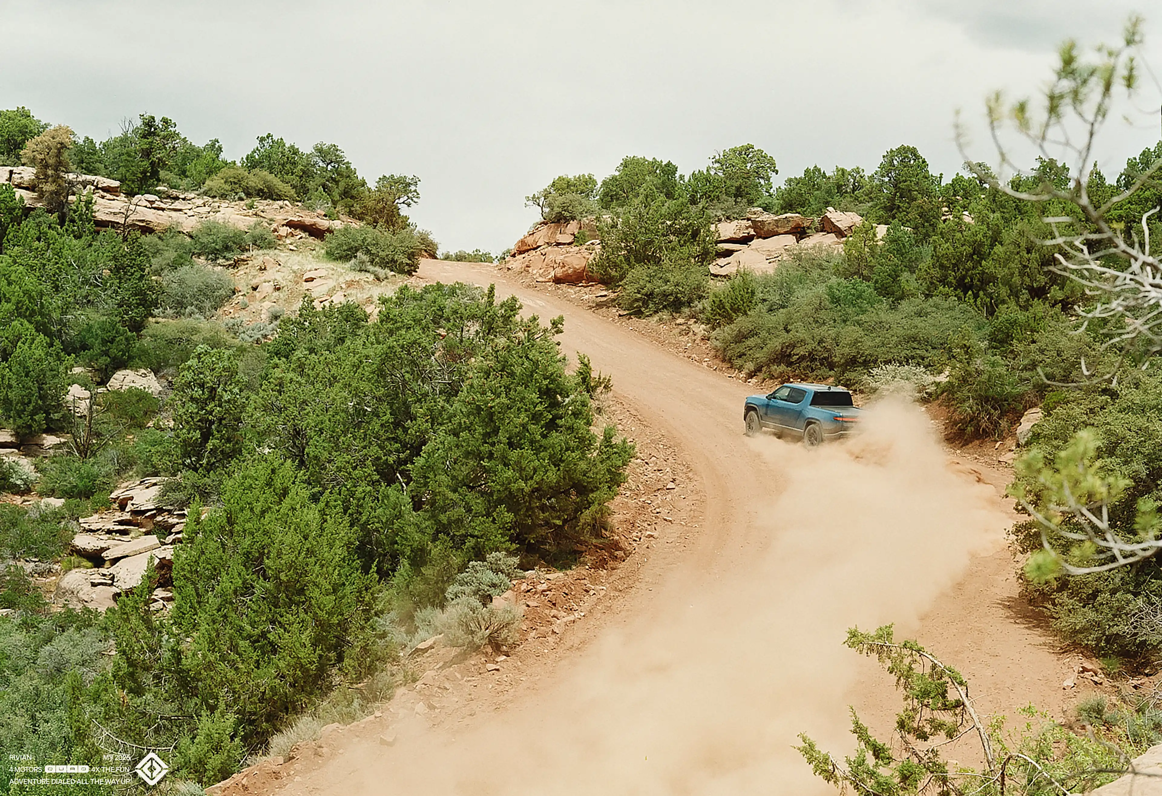 A Rivian R1T electric truck drifting a left turn as it drives up a dusty dirt road.