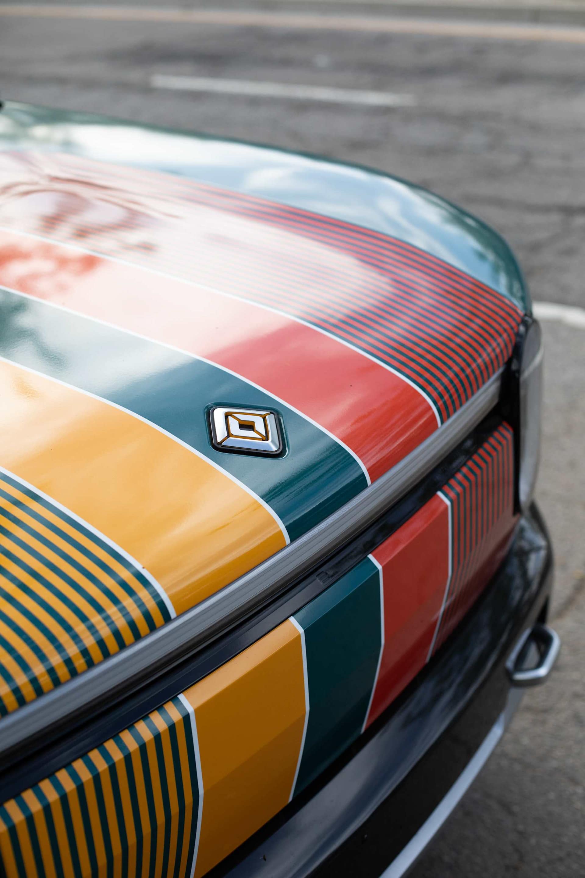 Close-up of the front of a Rivian vehicle with a custom paint job of horizontal stripes in orange, green, and red.