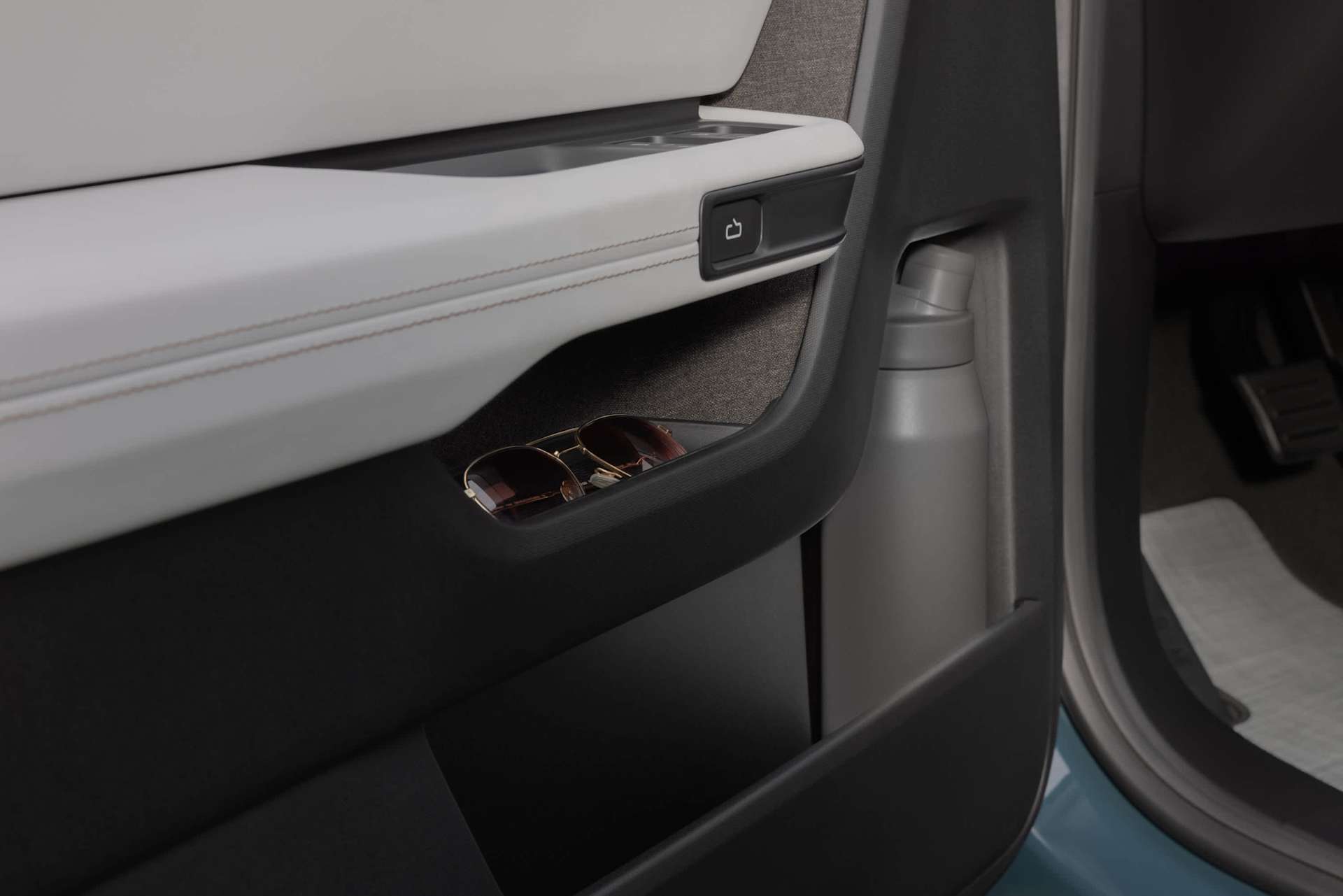 Close-up of a car door interior showing sunglasses in the pocket and a gray water bottle in the larger compartment.