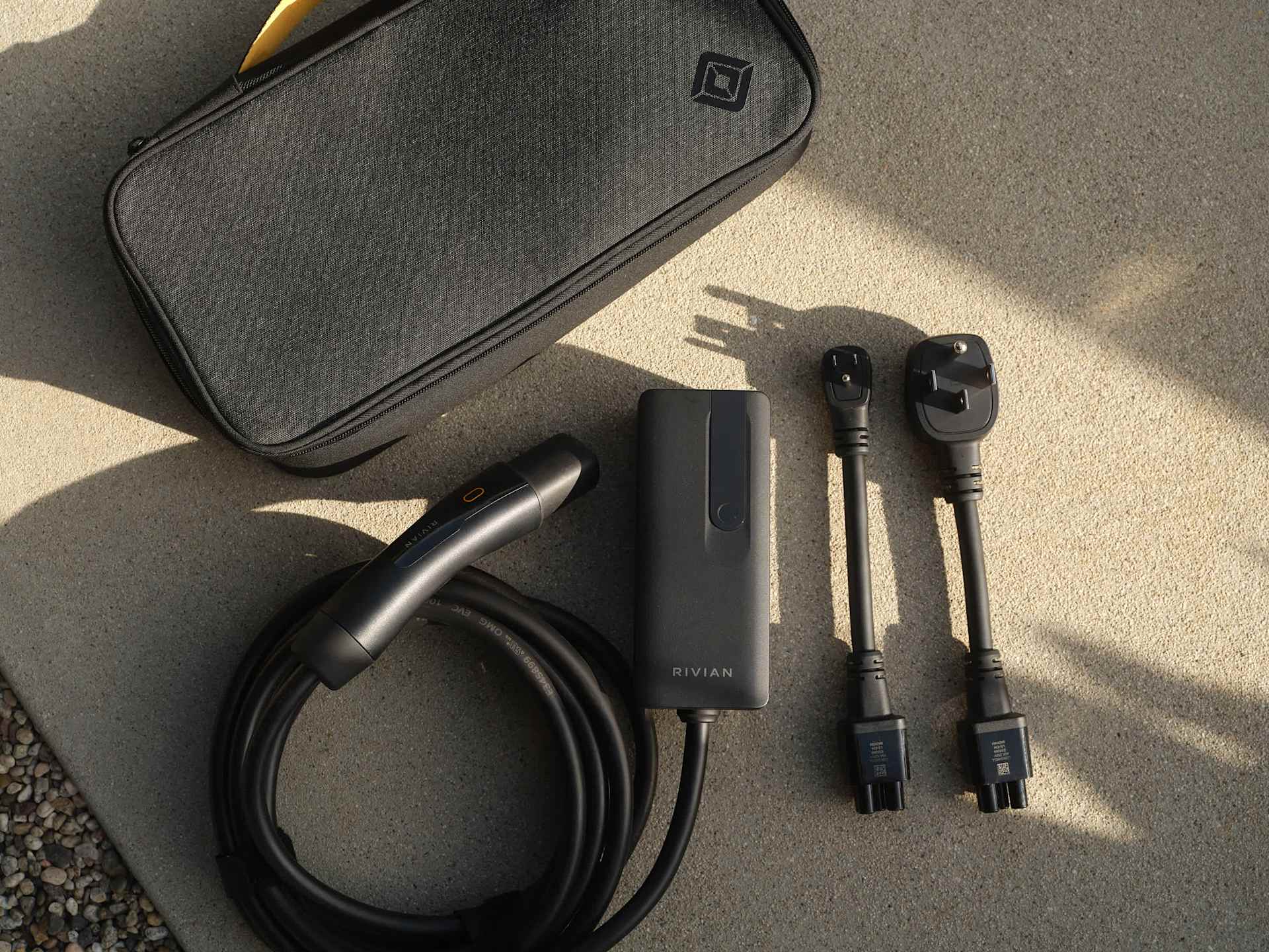 Rivian EV charger kit on concrete including charger, cable, two outlet adapters, and carrying case with Rivian logo.