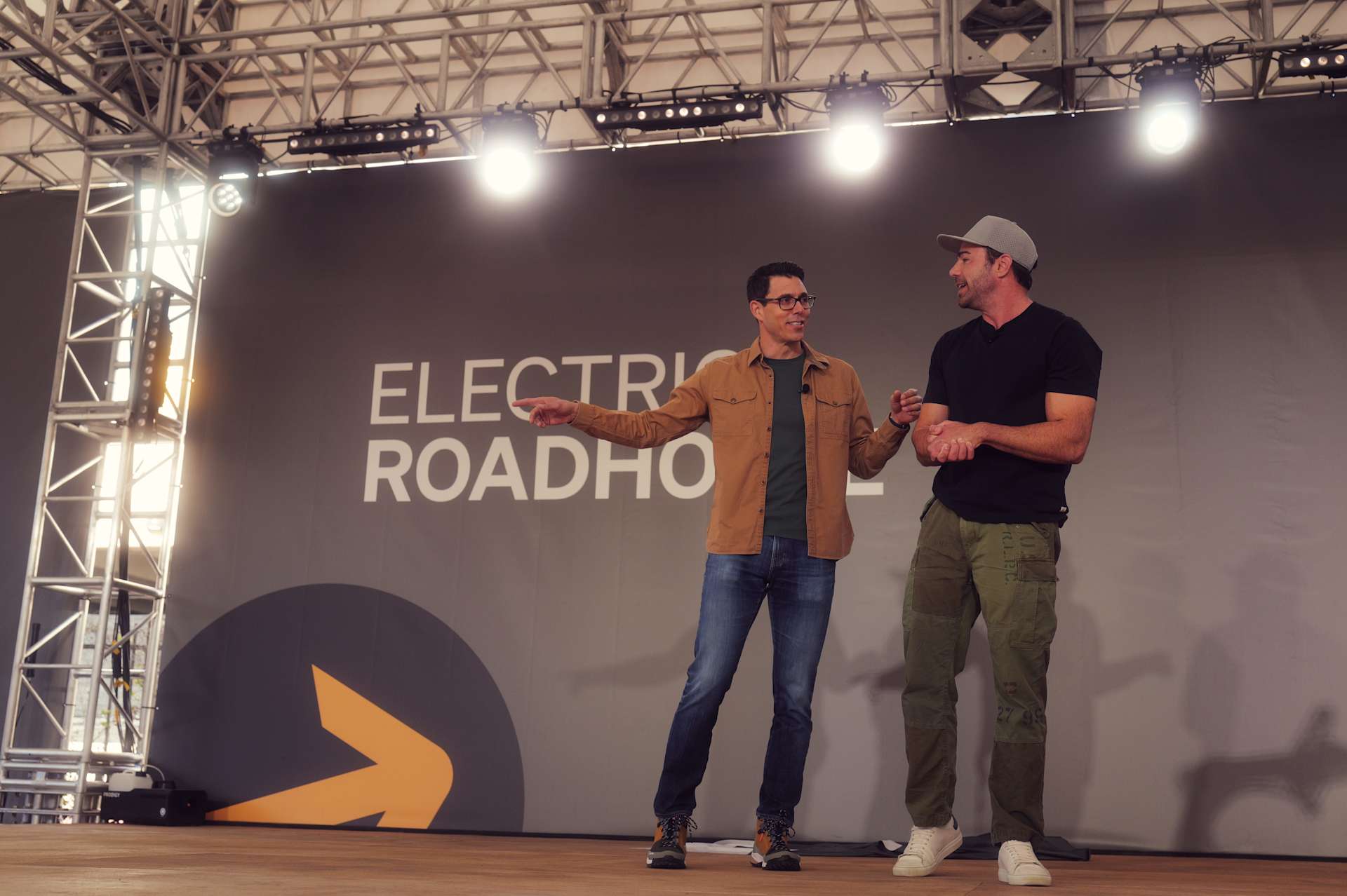 Two men stand on a stage at SXSW 2026, with "ELECTRIC ROADHO" visible on the backdrop. The man on the left gestures with his left hand. Stage lighting