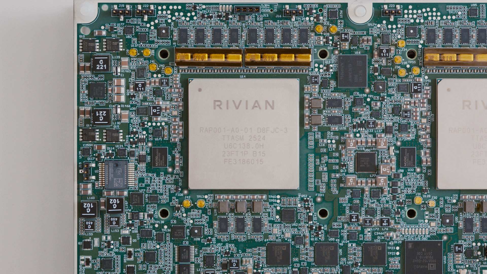 Close-up of a green Rivian circuit board with a central processor. The board is densely populated with electronic components and gold connectors. Text