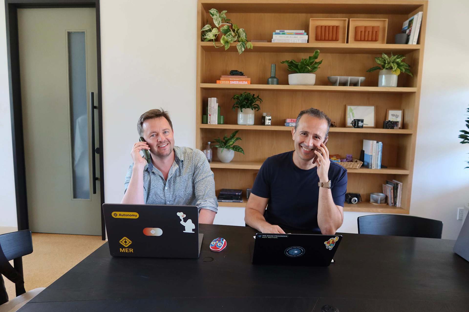 Wassym Bensaid conducts Reddit AMA. Two men sit at a table with laptops. The man on the left talks on a cell phone and smiles. The man on the right sm