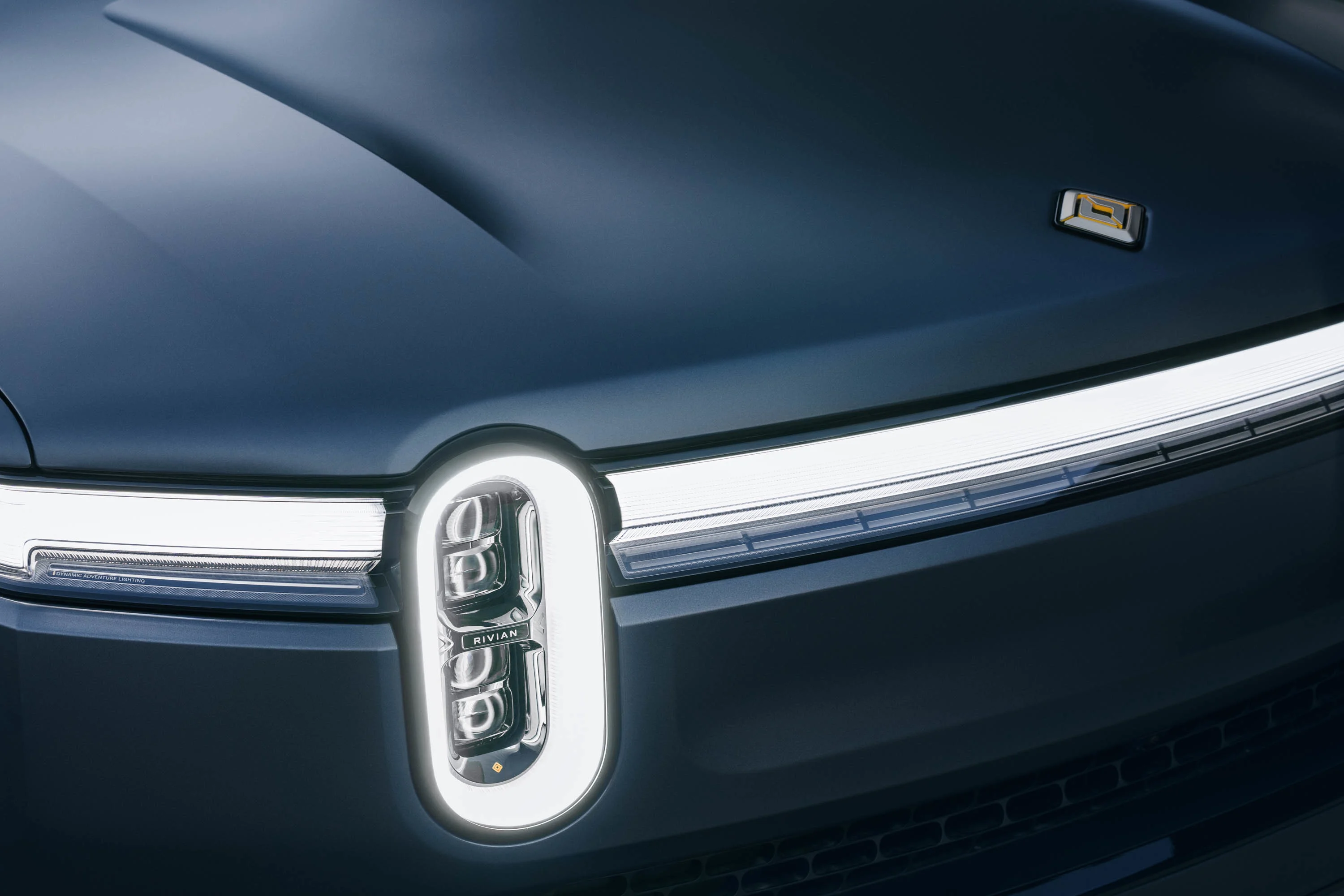 L'avant d'un véhicule électrique Rivian de couleur foncée, comprenant l'Ensemble Furtivité avec une protection de peinture XPEL, des accents sombres et des roues noires