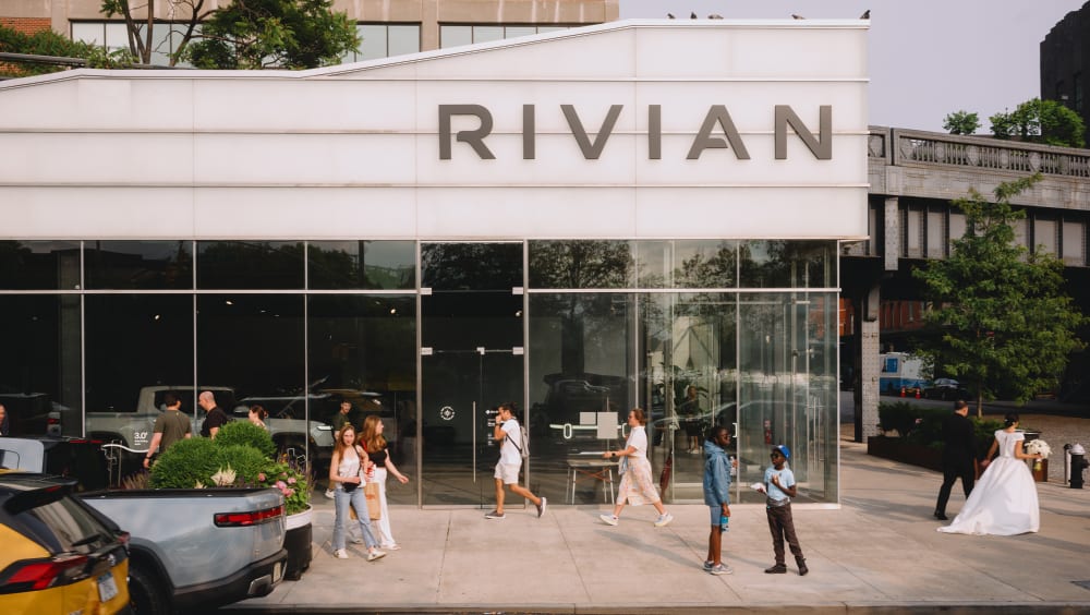 Children sitting on the tailgate of an R1S look at the screen of a tablet.